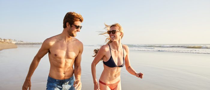 Smiling young couple in swimwear running together along a sandy beach on a sunny summer afternoon